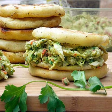 Arepas stuffed with chicken avocado salad, and a stack of five arepas in the background.