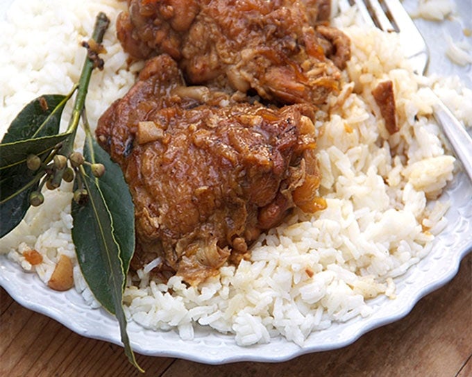 A plate of Filipino Chicken Adobo over rice with a sprig of fresh bay leaves