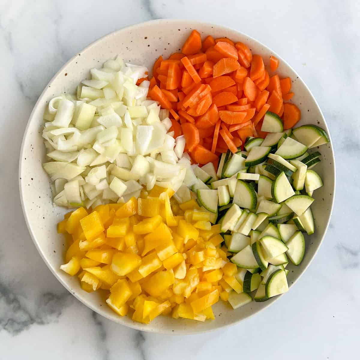 4 piles of chopped veggies in a bowl: carrots, zucchini, onions and yellow bell pepper.