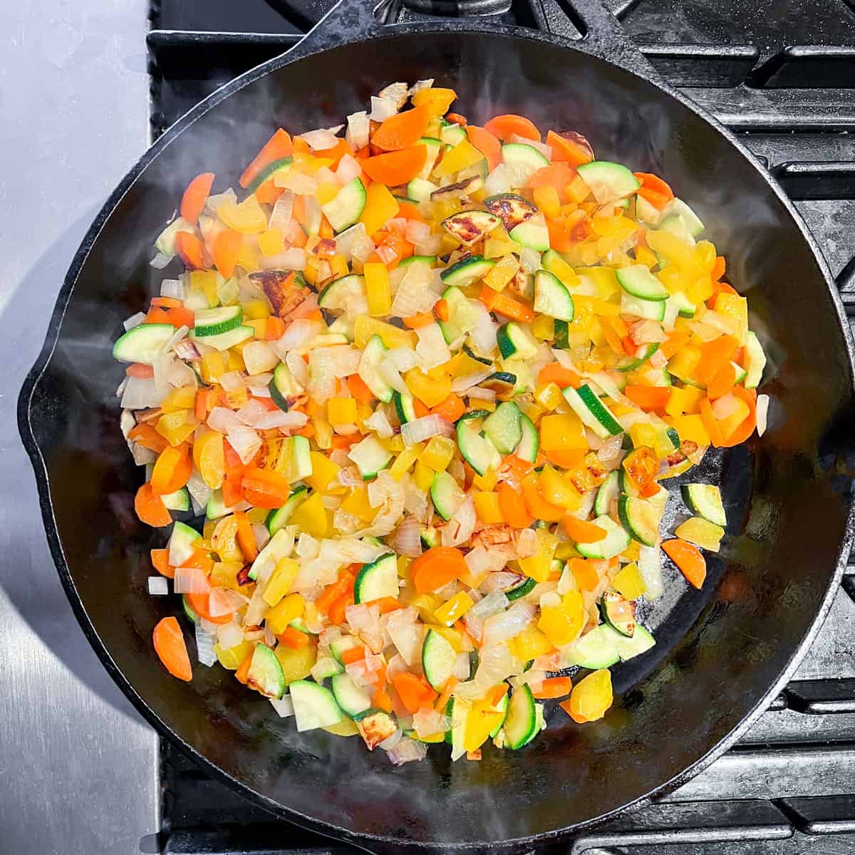chopped carrots, onions, zucchini and yellow peppers cooking in a cast iron skillet.