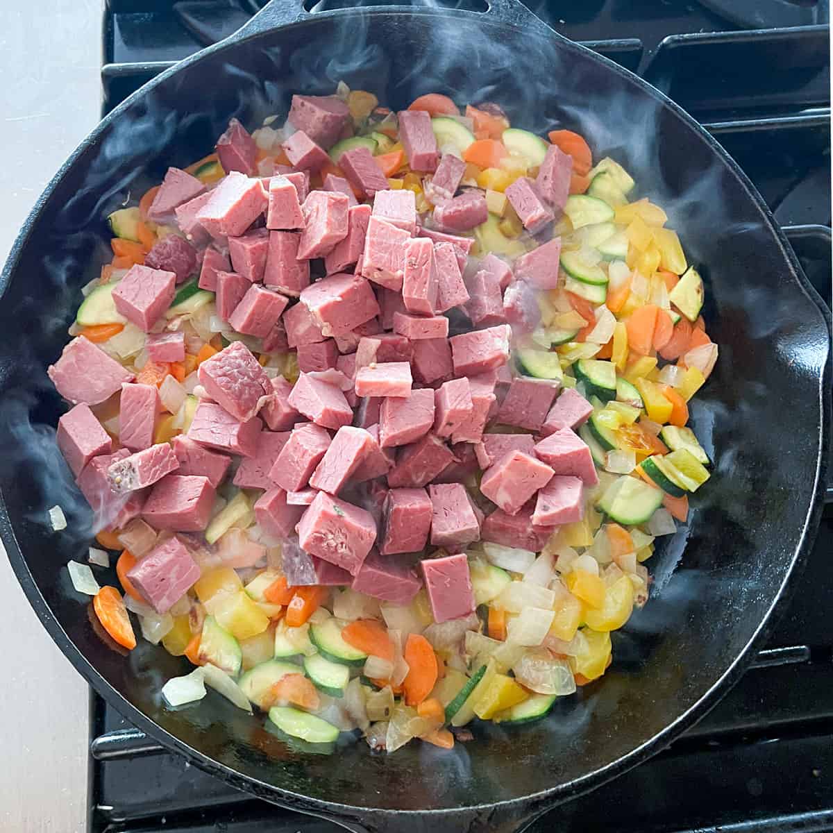 Cubed corned beef on top of sautéed veggies, in a cast iron skillet.