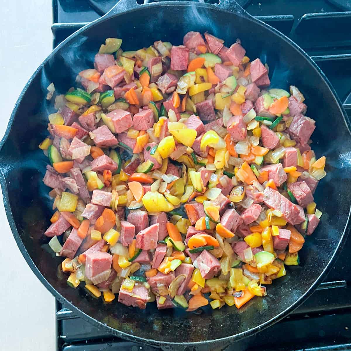 cubes of corned beef and sautéed veggies in a cast iron skillet.