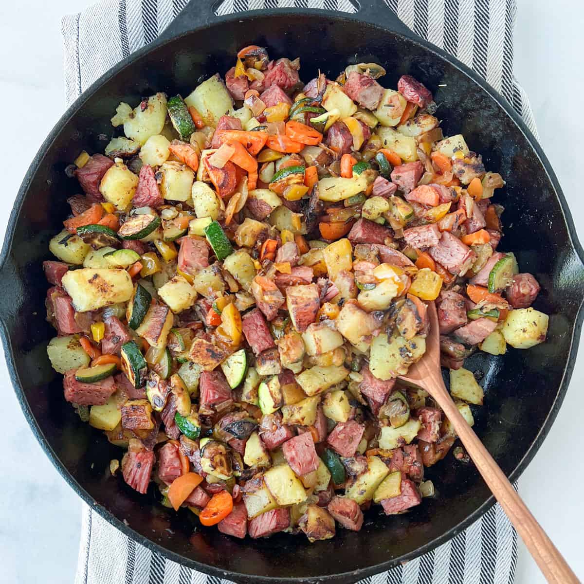 Corned beef has in a cast iron skillet with a wooden spoon.