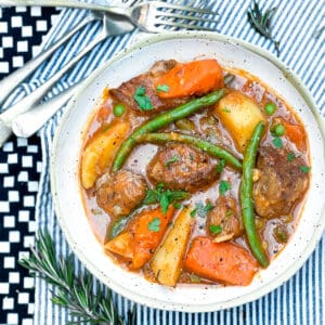 Bowl of lamb stew with green beans, peas, chunks of carrots and potatoes.