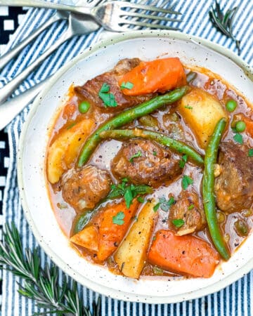 Bowl of lamb stew with green beans, peas, chunks of carrots and potatoes.