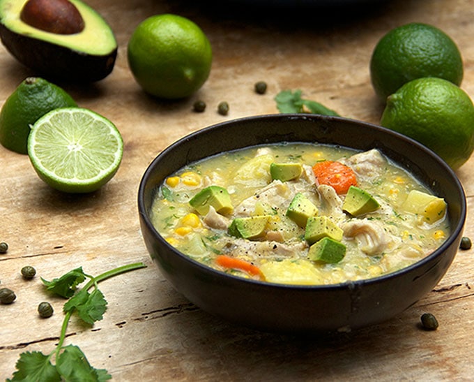 Bowl filled with thick rich chicken soup that has lots of shredded chicken, corn, potatoes and cubes of avocado on top