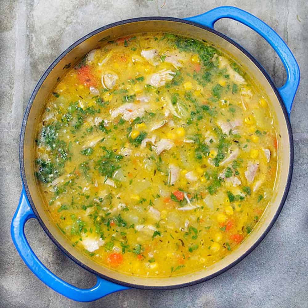Dutch oven filled with chicken soup that's loaded with shredded chicken, corn kernels and cubed potatoes