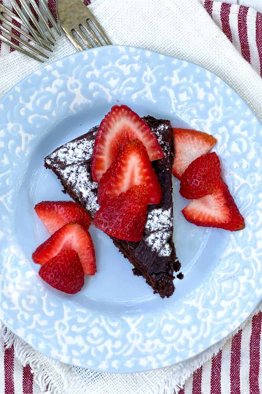 slice of flourless chocolate cake topped with sliced strawberries on a light blue plate