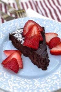 slice of flourless chocolate truffle cake on a light blue plate with sliced strawberries on top and on the sides