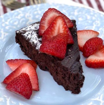 slice of flourless chocolate truffle cake on a light blue plate with sliced strawberries on top and on the sides