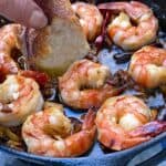 8 shrimp in a skillet with bread being dipped into the garlicky oil