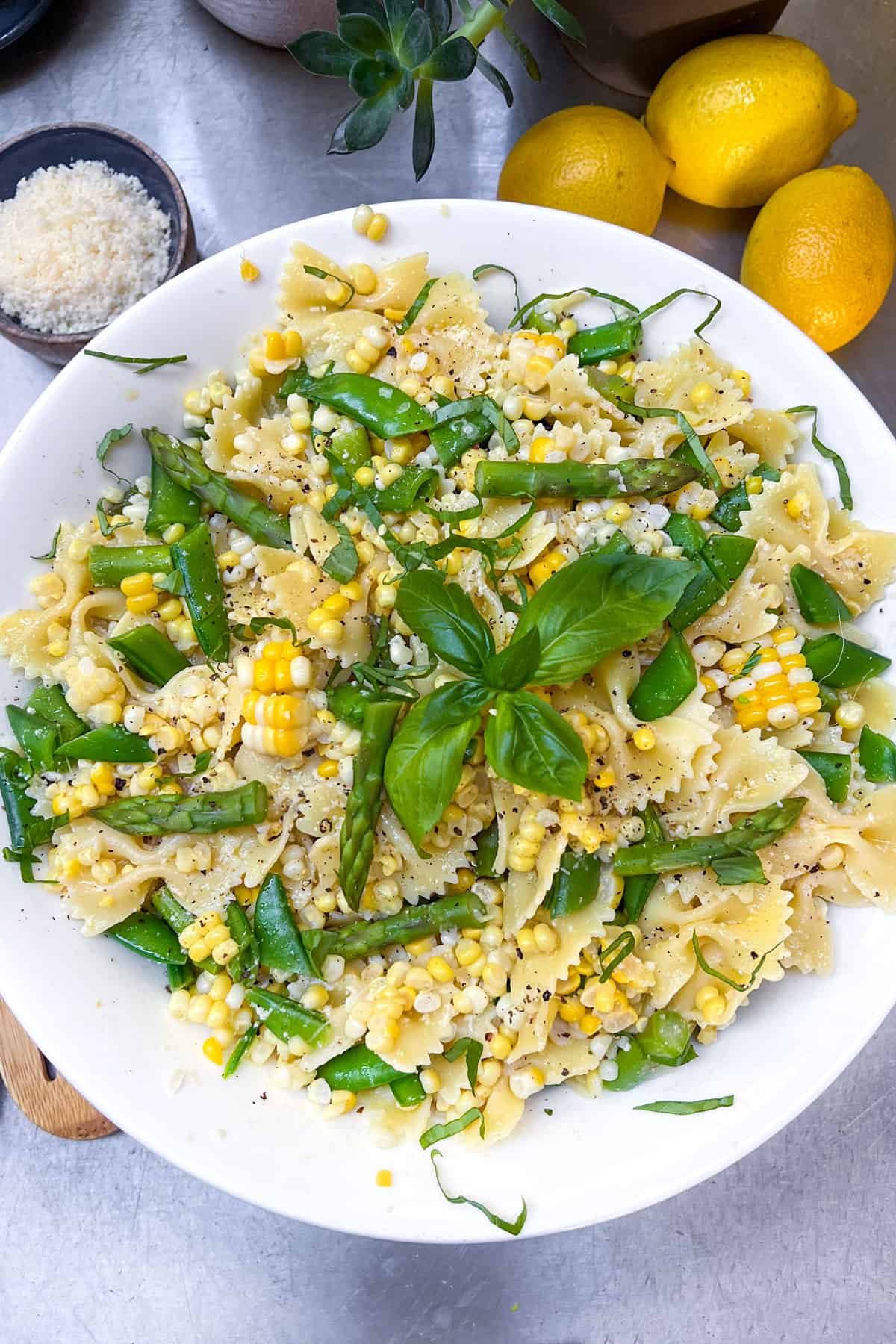 serving bowl filled with butterfly pasta tossed with fresh corn, sliced sugar snap peas and bite sized pieces of asparagus.
