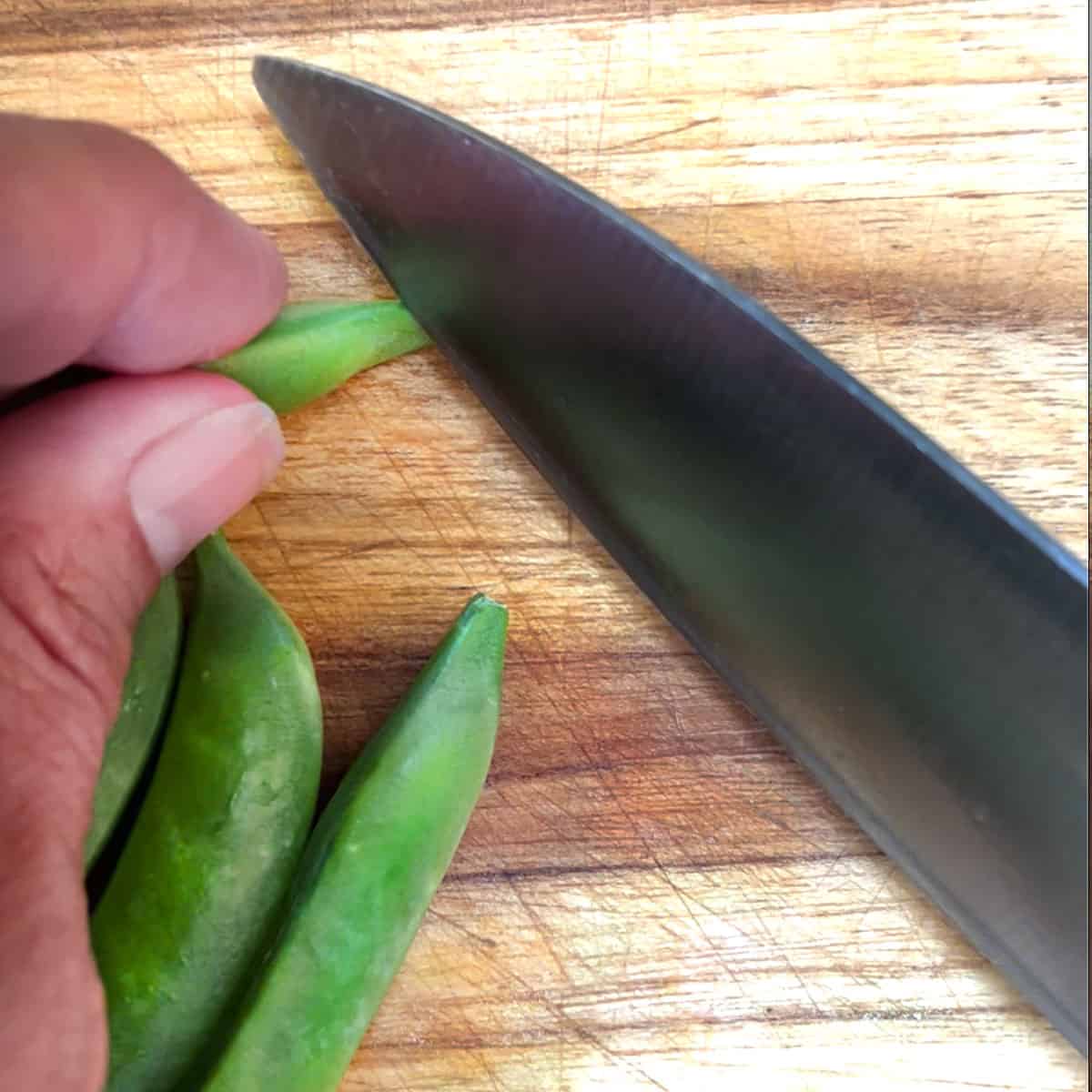 knife cutting the tip of a snap pea off.