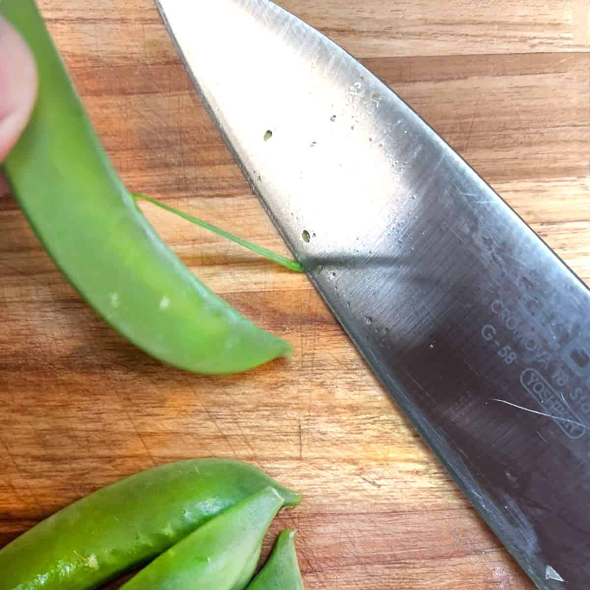Pulling a snap pea away from a knife to remove the string.