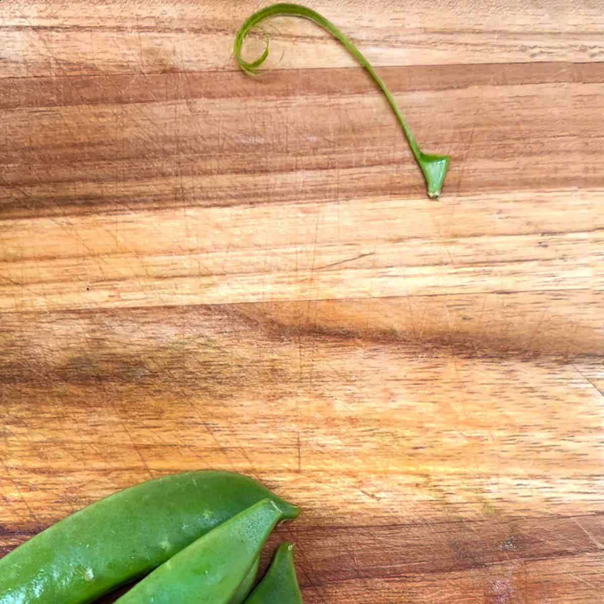 The hard stem end of a sugar snap pea connected to the stringy fiber after they've been removed from the pea. 