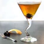 Perfect Manhattan cocktail in a martini glass with a piece of orange zest on the counter and a cherry