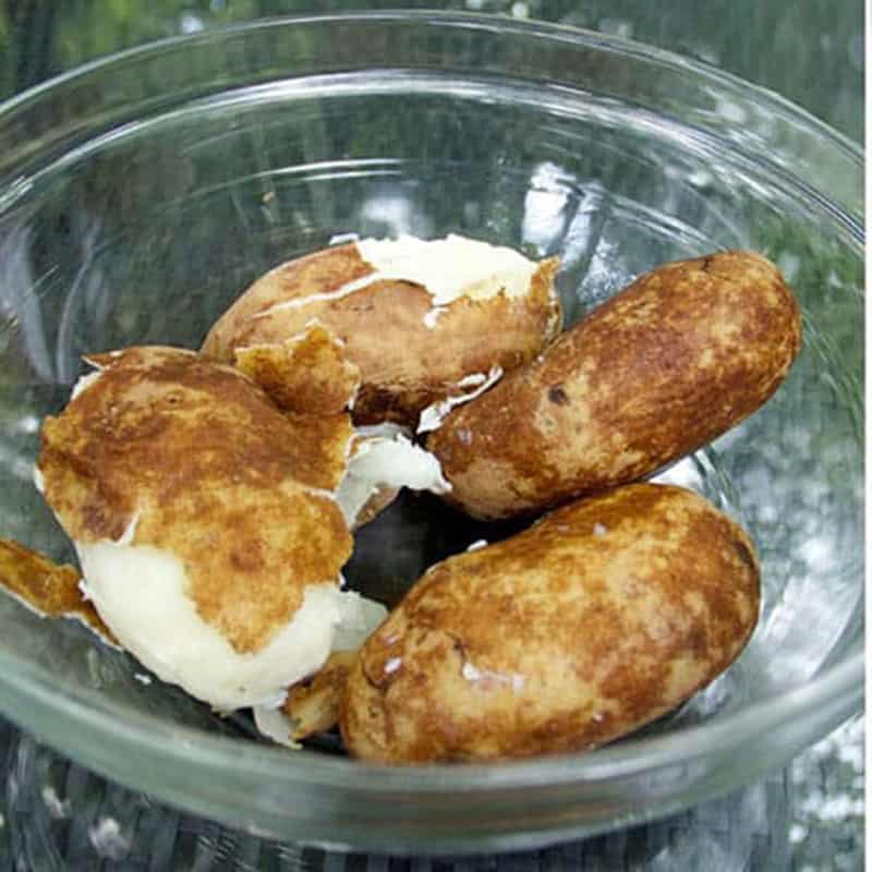 4 boiled russet potatoes in a glass bowl, their skins loosened by boiling