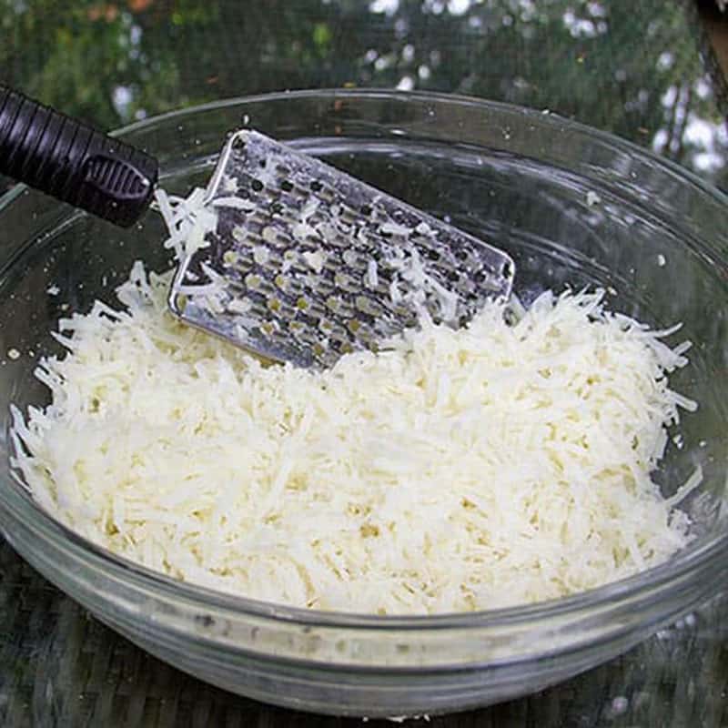 shredded potatoes in a glass bowl with a cheese grater in the bowl.
