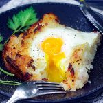 one slice of Swiss Rosti on a black plate - shredded potato casserole with an egg baked on top