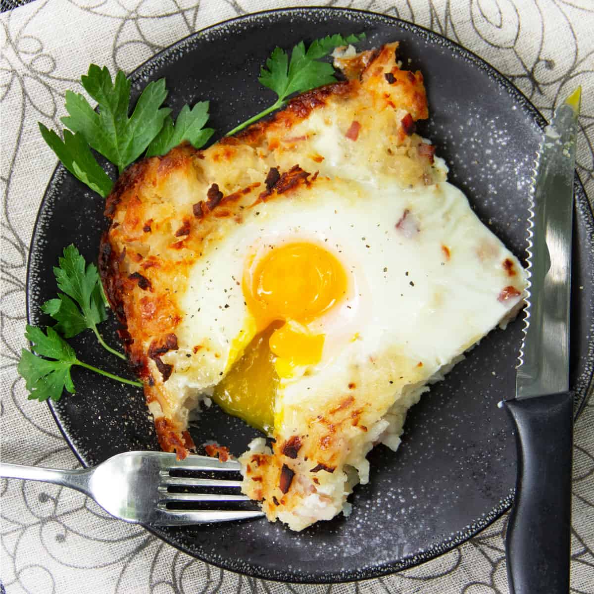 a square piece of shredded potato casserole (rosti) with a fork and some egg yolk dripping down