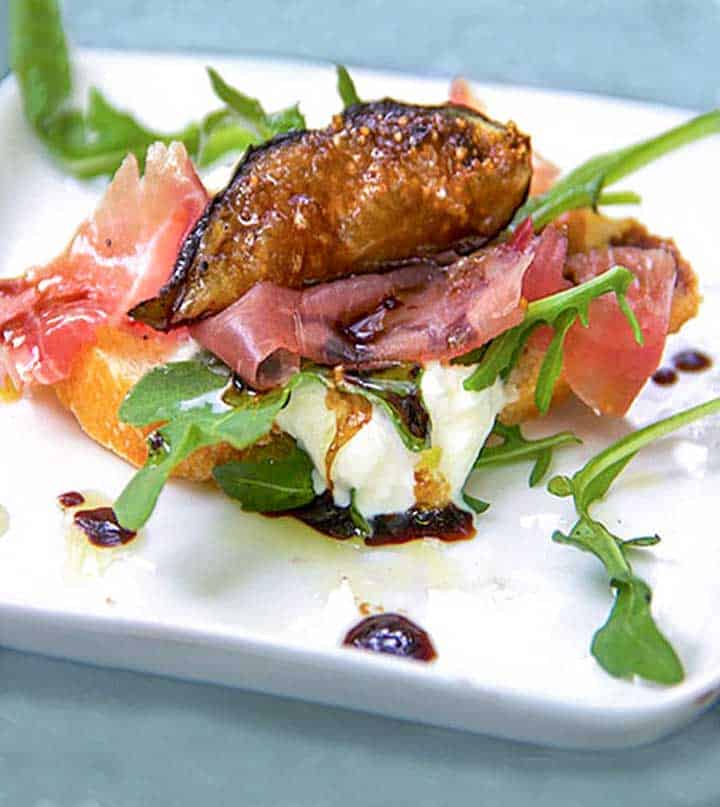 one piece of grilled fig, prosciutto and burrata bruschetta, on a small square white plate