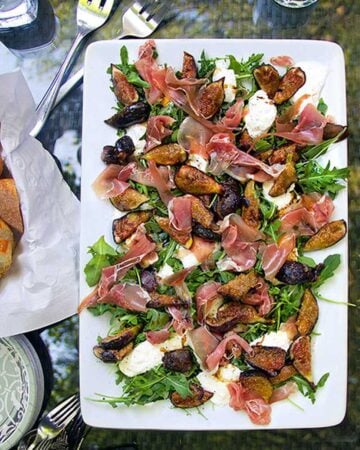 white rectangular platter topped with grilled figs, prosciutto and burrata and arugula