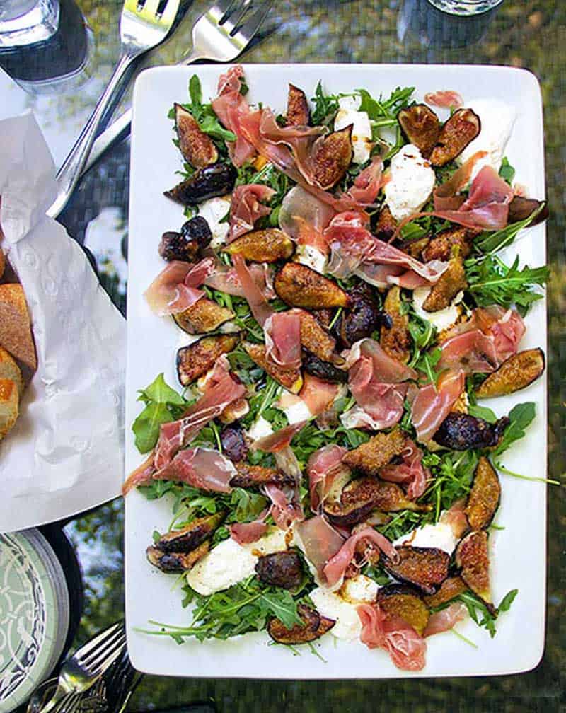 white rectangular platter topped with grilled figs, prosciutto and burrata and arugula