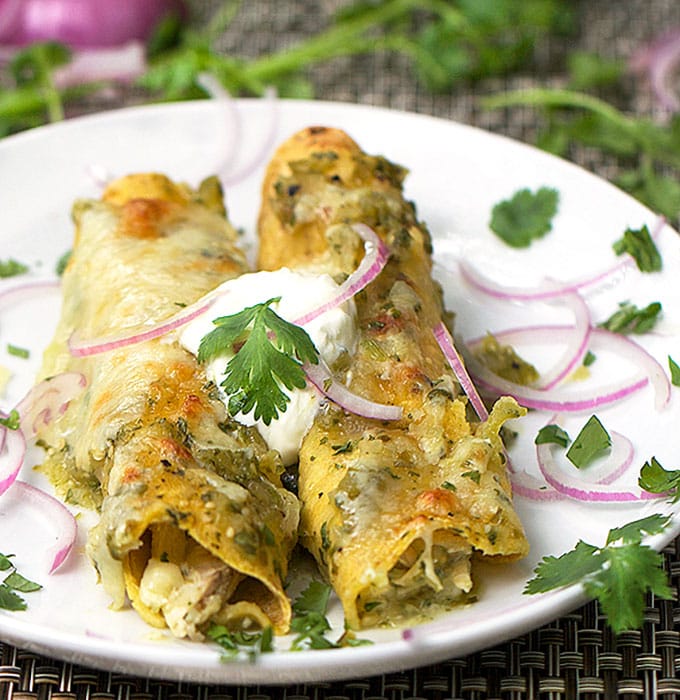 Two chicken enchiladas verdes on a plate, topped with sour cream, red onions and cilantro