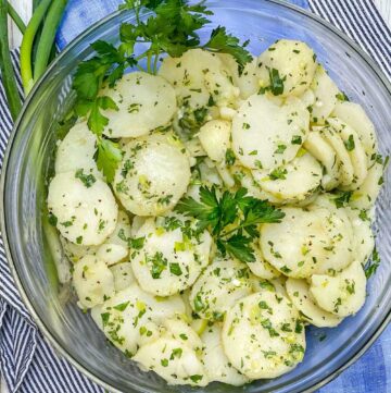 Close up looking down into a bowl of french potato salad, garnished with parsley sprigs
