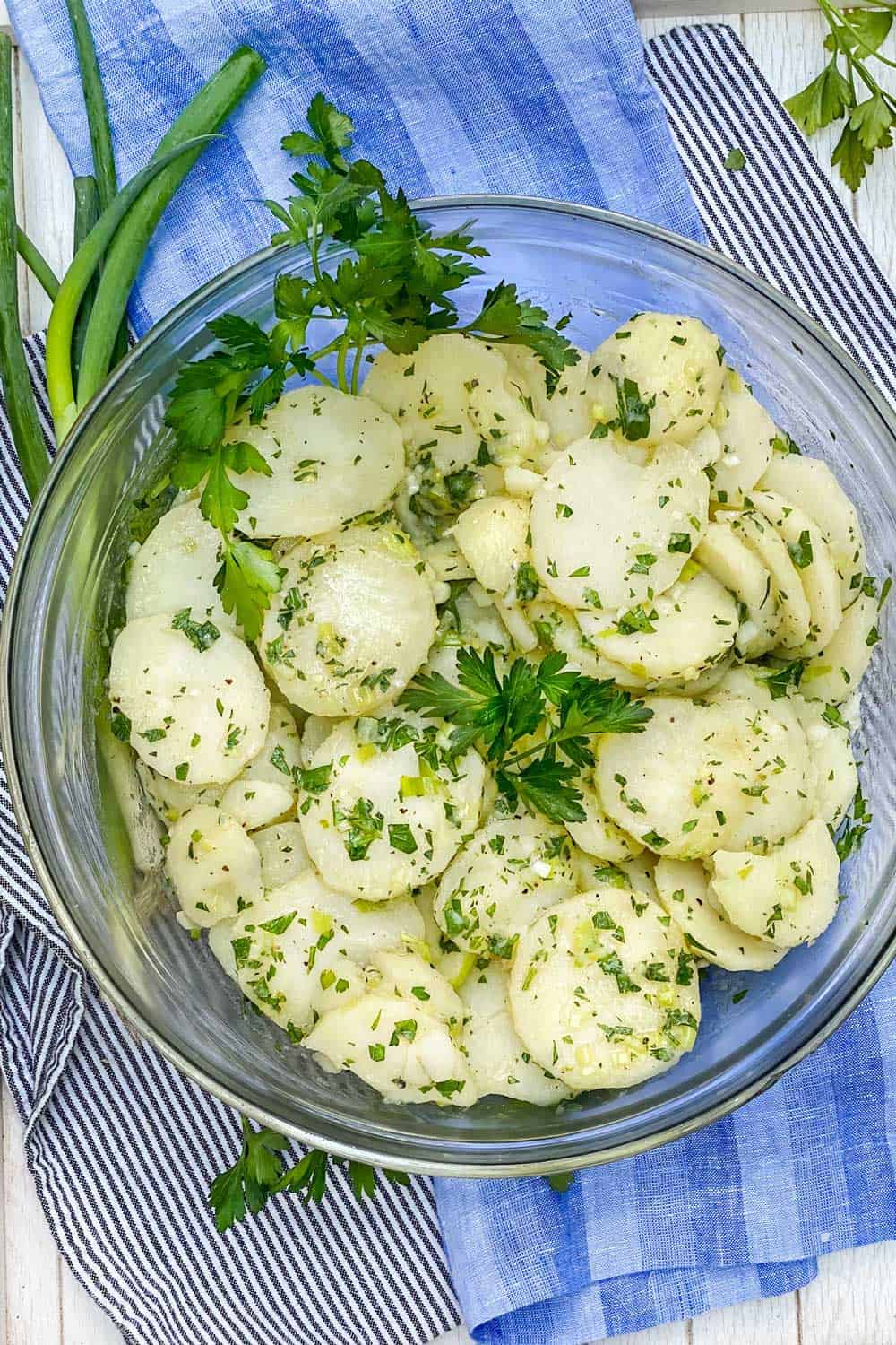 Close up looking down into a bowl of french potato salad, garnished with parsley sprigs