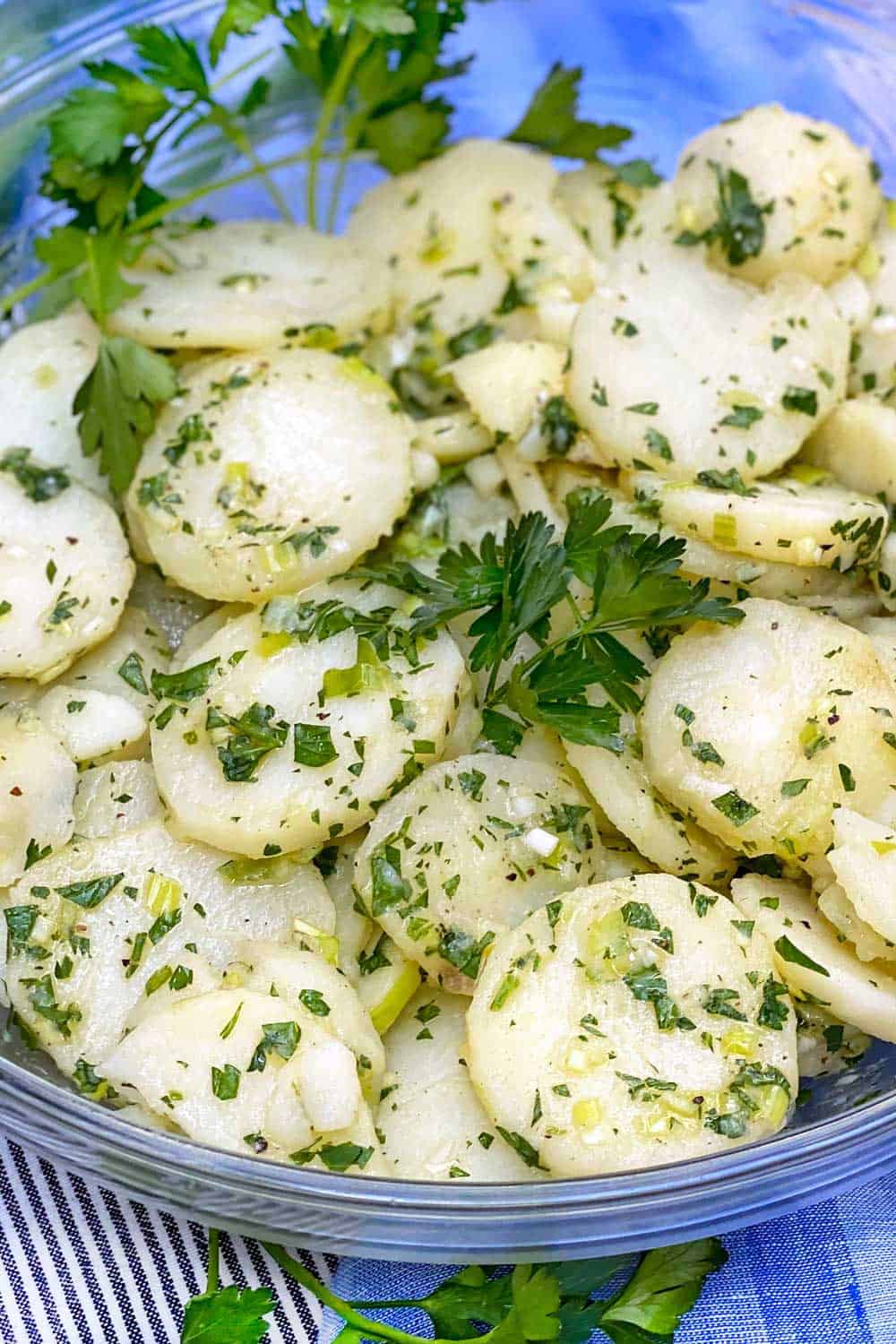 Close up looking down into a bowl of french potato salad, garnished with parsley sprigs