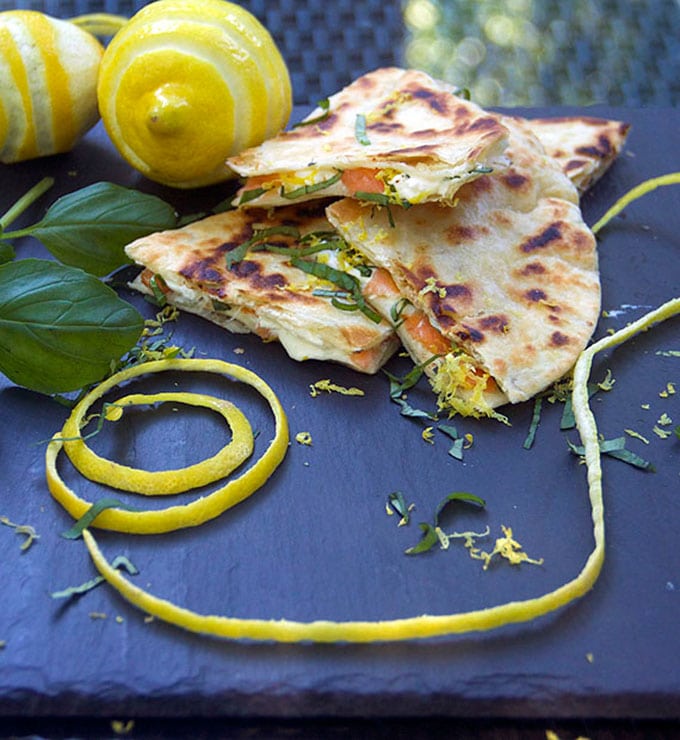 slate serving board with stripe-cut lemons, a big swirl of lemon rind and three triangular slices of smoked salmon quesadills 