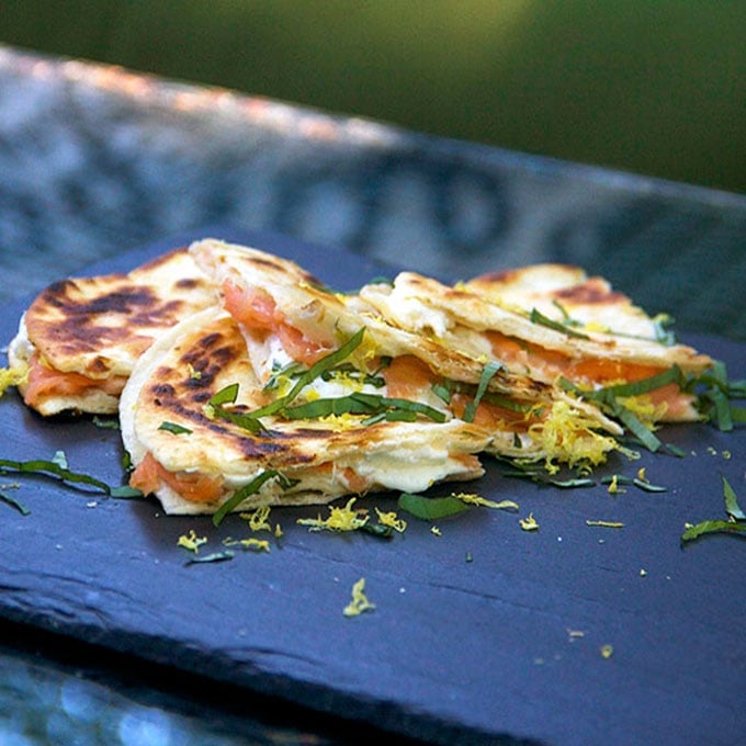 slate serving board topped with three triangular slices of smoked salmon quesadillas with goat cheese, lemon zest and slivered basil.