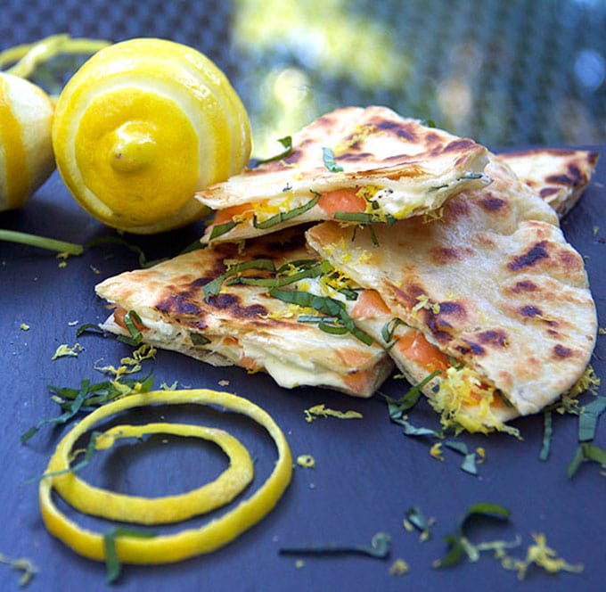 triangles of smoked salmon quesadillas with goat cheese with a coil of lemon peel on and a zested lemon and a confetti of slivered basil and lemon zest