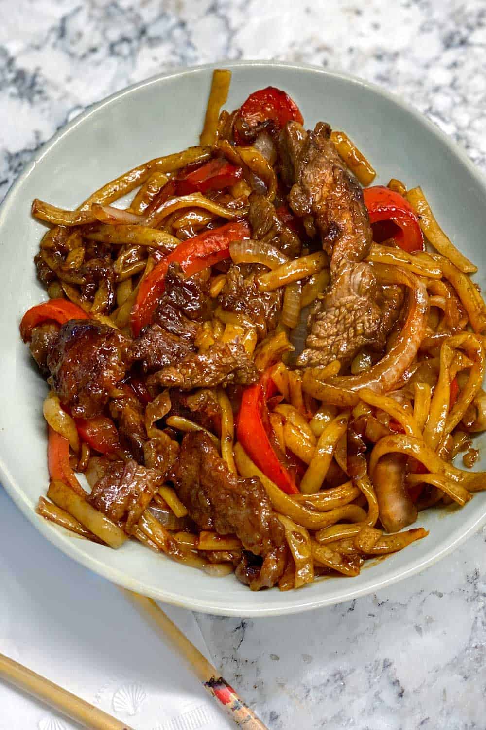 close up looking down into a bowl of beef chow fun noodles with strips of red bell pepper