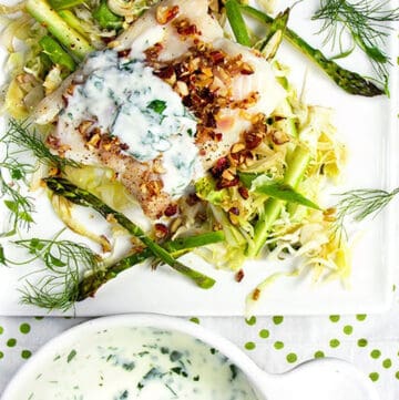 a fillet of baked haddock on a bed of shredded vegetables, topped with yogurt sauce and almond gremolata