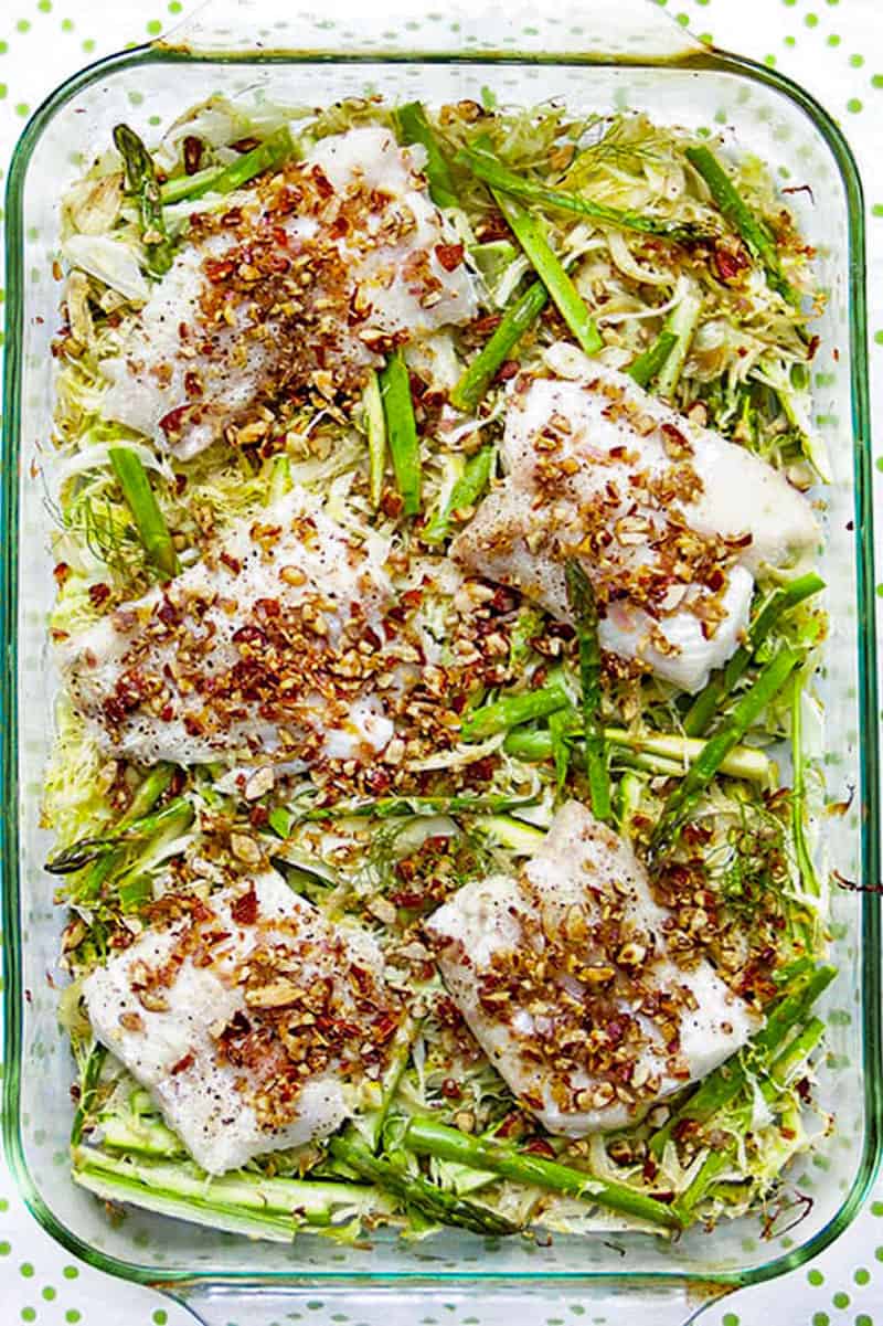 rectangular glass baking dish with 5 fillets of haddock on top of shredded vegetables and topped with almond gremolata