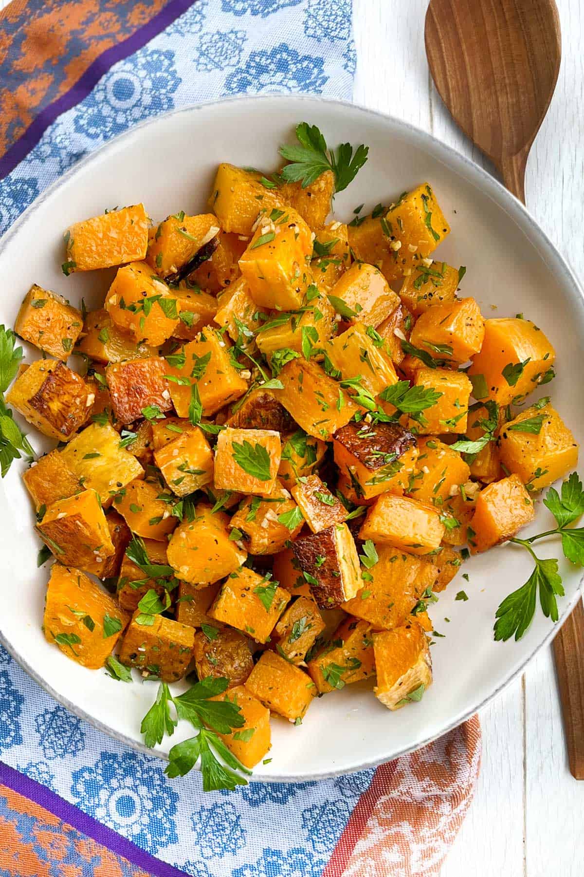 Cubes of roasted butternut squash in a white bowl, topped with parsley garlic oil