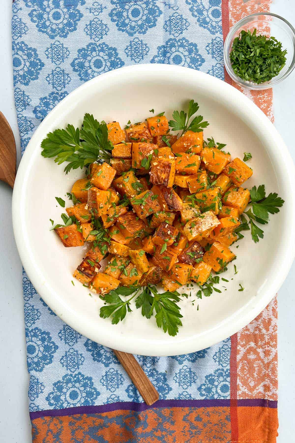cubes of roasted butternut squash in a white bowl, decorated with sprigs of parsley