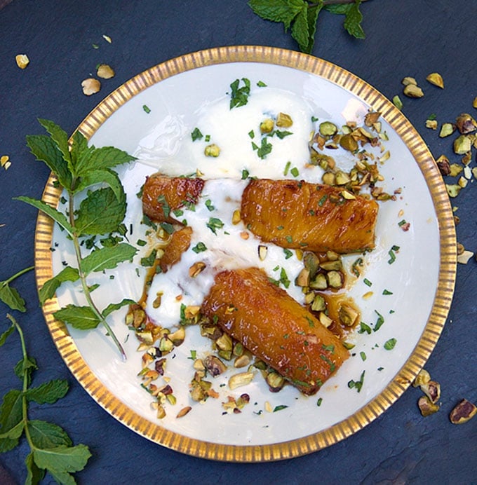 gold rimmed dessert plate with two piece of honey roasted pineapple topped with yogurt, chopped pistachios and chopped mint