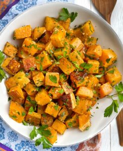 Cubes of roasted butternut squash in a white bowl, topped with parsley garlic oil