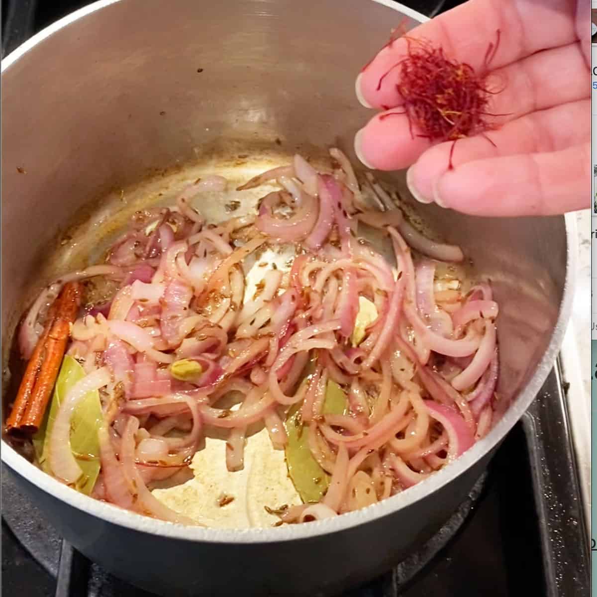small saucepan with whole spice; cinnamon, cardamom, bay leaves, and sliced red onions, and a hand holding a pile of saffron threads.