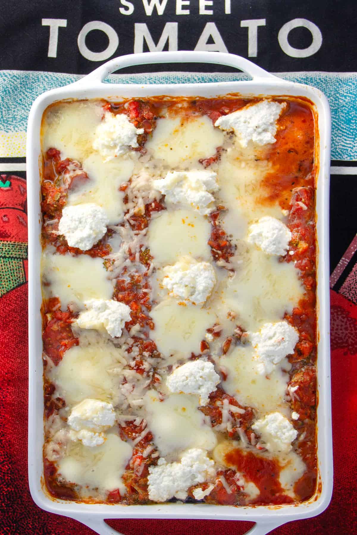 Rectangular casserole filled with eggplant lasagna, melting mozzarella on top with blobs of fluffy ricotta cheese and a sprinkling of parmesan.