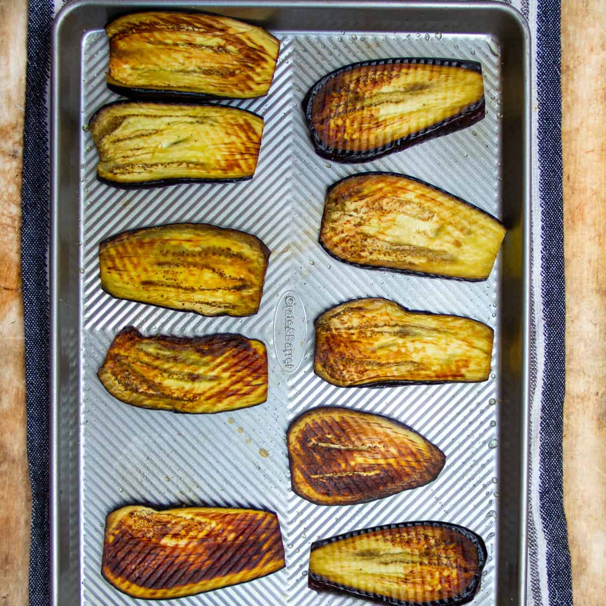about a dozen thin slices of roasted eggplant on a rimmed baking sheet.