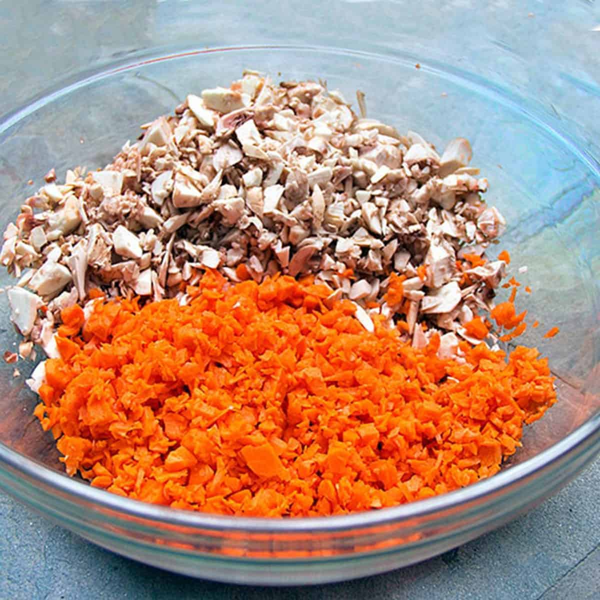 Glass mixing bowl filled with finely chopped carrots and mushrooms