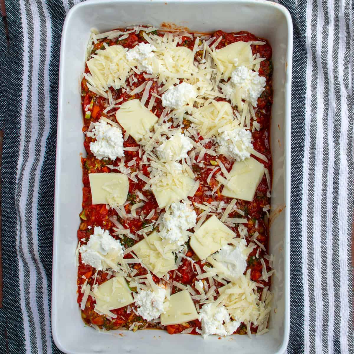rectangular casserole filled with a layer of tomato sauce and three lasagna cheeses.