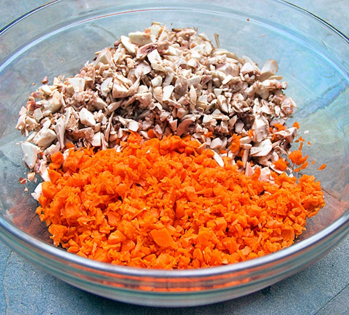 a glass bowl filled with chopped carrots and chopped mushrooms
