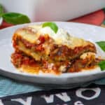 One piece of saucy cheesy eggplant lasagna on a small plate topped with a basil leaf.