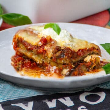 One piece of saucy cheesy eggplant lasagna on a small plate topped with a basil leaf.