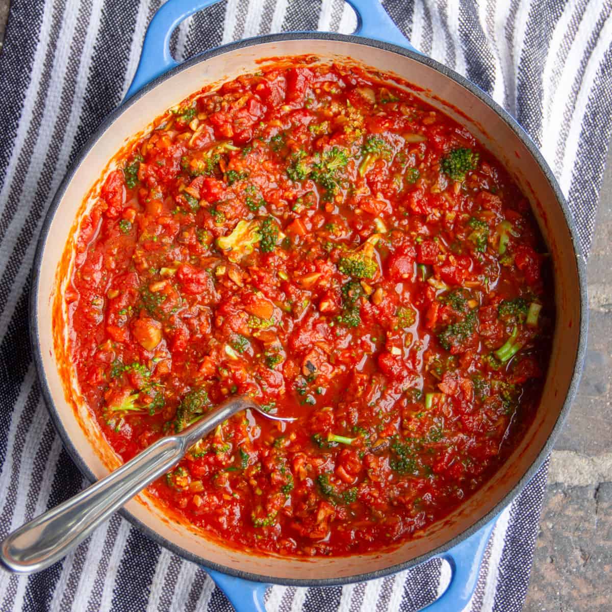 Thick primavera tomato sauce in a round dutch oven with a metal serving spoon stuck in.